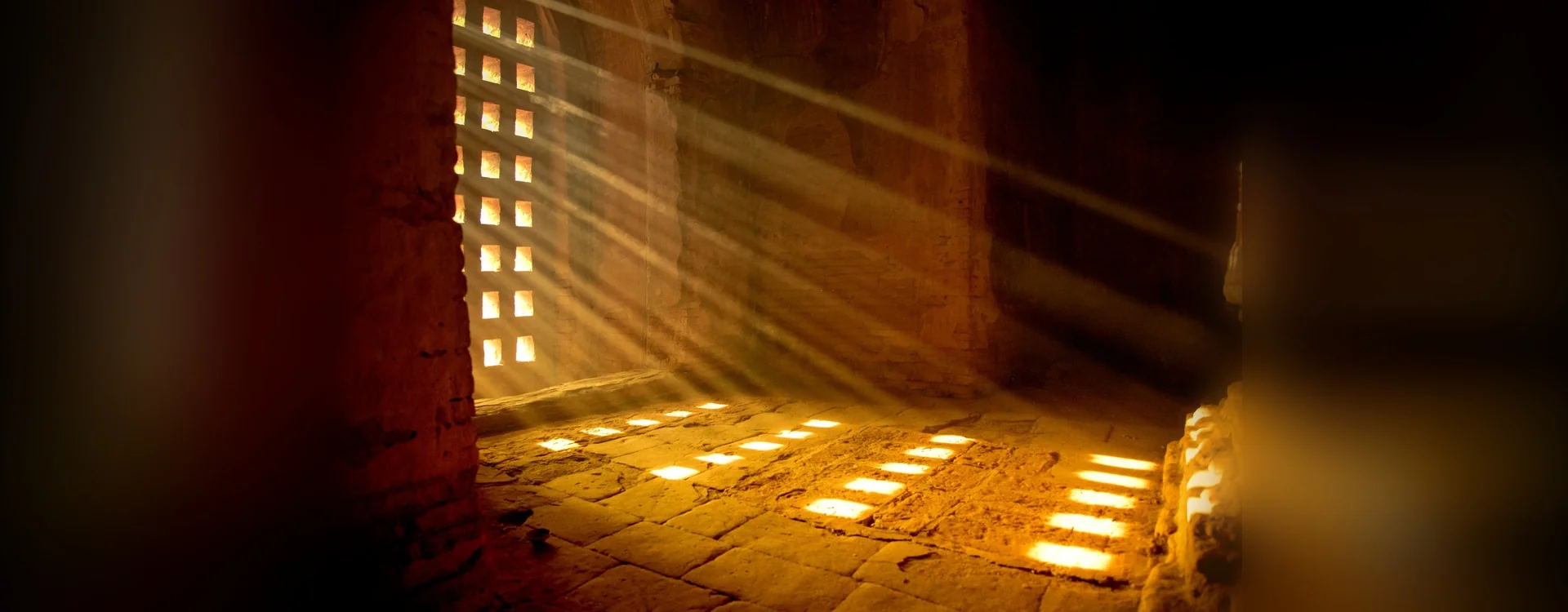 Haces de luz que entran por una celosía de piedra en el interior en penumbra de un templo antiguo