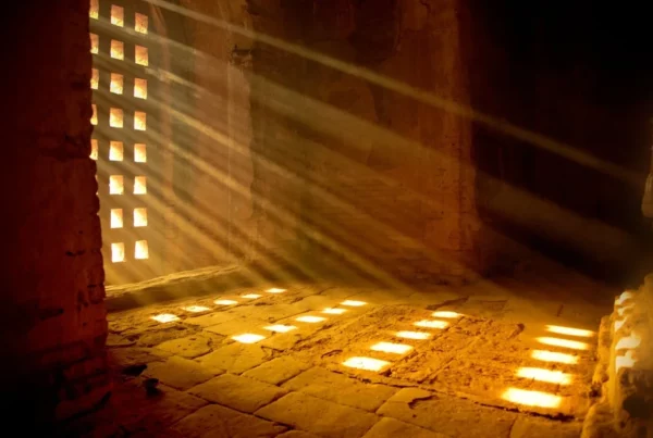Rayos de sol atravesando una celosía y dibujando cuadrados de luz sobre el suelo de piedra de un templo